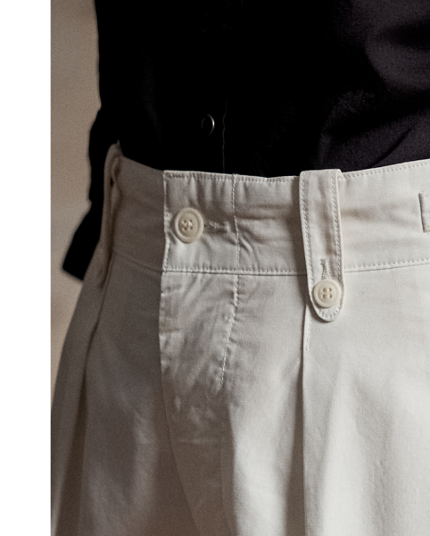 Cropped trousers made with cotton poplin. Inspired by 1940s trousers. Stitched-down pleated front. Buttoned belt loops. Adjustable buckled tabs at the waist. Sanforized to minimise shrinkage.