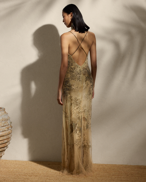 Featuring a bias-cut slip silhouette with crisscross straps, the Kacey's dual-layer design combines exquisite fabrics with fine craftsmanship. First, the silk gauze interior layer is printed with the season's dreamy floral motif, which originated as a watercolour painting done by one of Ralph Lauren Lauren's skilled artists. Layered with netting lace on the exterior, the outer layer is embroidered by a team of six specialised artisans using a traditional Aari technique, carefully arranging a collection of cut glass beads in a dégradé placement to highlight this style's romantic pattern.