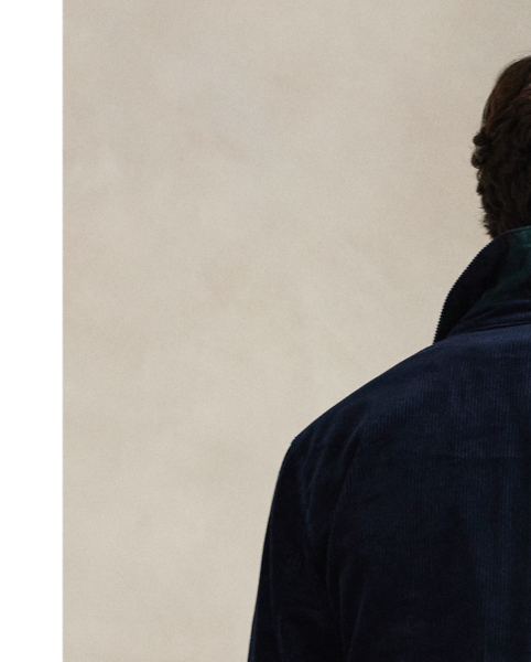 This cotton jacket contrasts the sporty silhouette of a windbreaker with the rustic texture of wide-wale corduroy. It is dyed in a custom-developed colour and finished with considered details, such as tartan-inspired lining and leather accents.