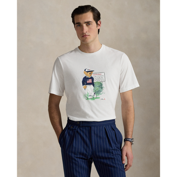Designed for our 2025 US Ryder Cup Team Collection, this cotton jersey T-shirt features our beloved Polo Bear wearing a version of our Iconic Flag Jumper, which we updated specifically for the players' uniform. Behind our mascot is the famous sign at Bethpage Black Golf Course, which cautions players of its immense difficulty and is a landmark at the location of this year's tournament. Many start their rounds with a photo by the sign – now a nationally known symbol, as our Polo Bear does here.